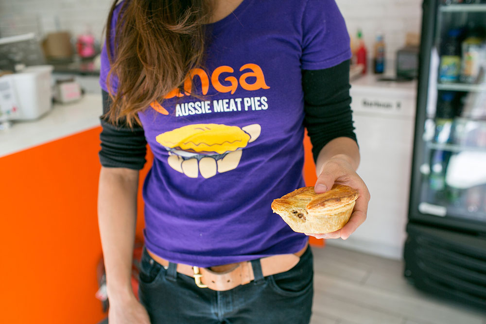 A woman in a Kanga Pies t-shirt holds a pie