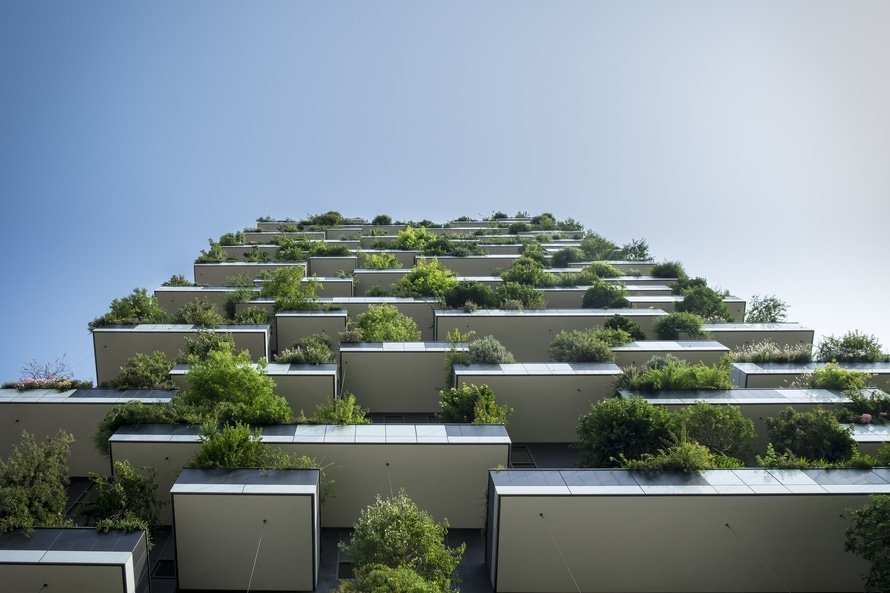 Looking up at tall building's patio spaces with greenery growing over all of it