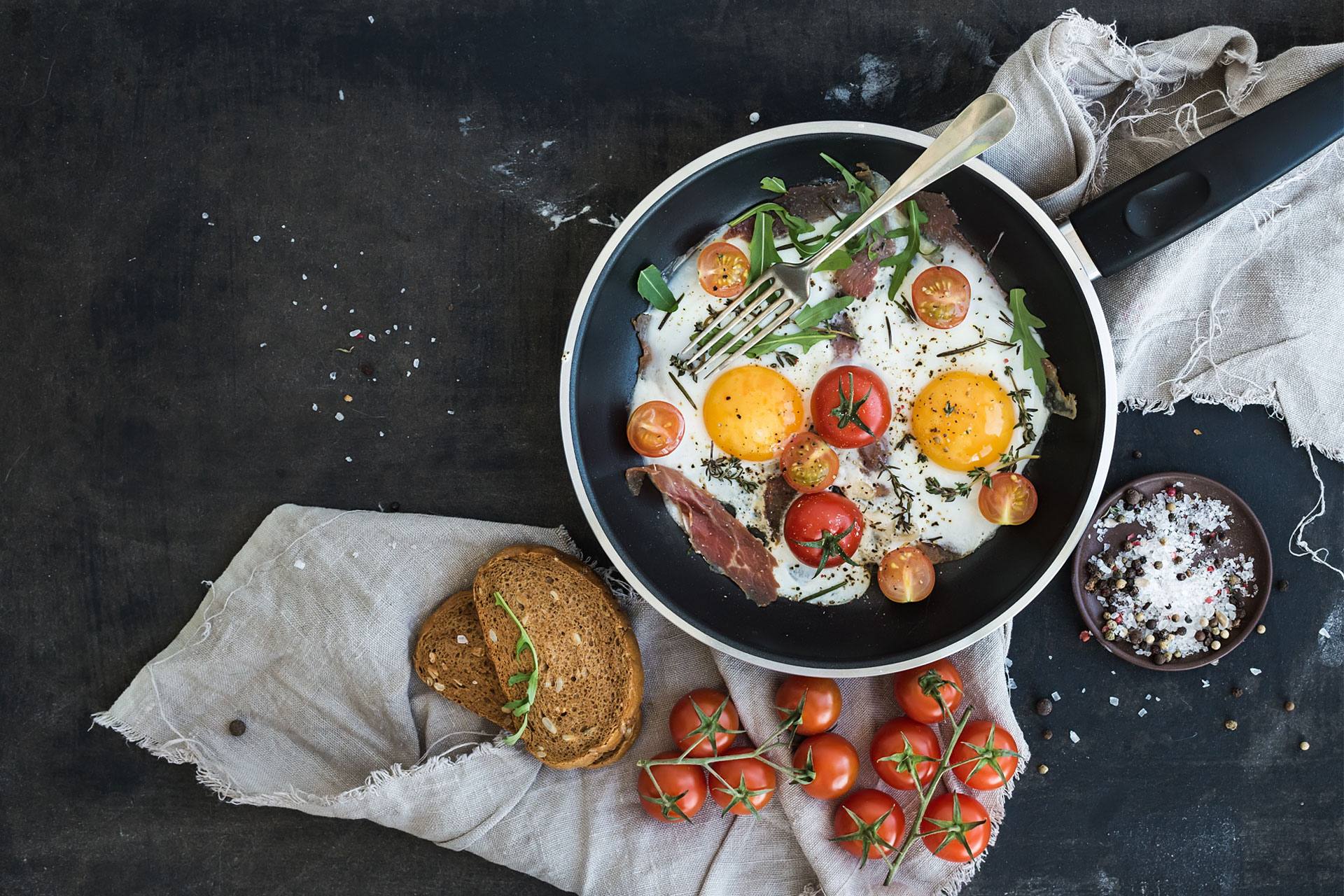 Eggs in a pan next to cherry tomatoes on a counter