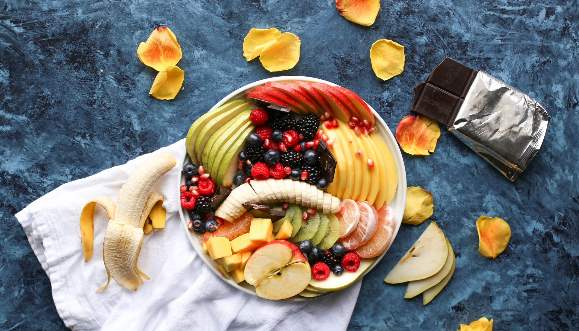 Healthy breakfast bowl of tropical fruit on a countertop next to an open dark chocolate bar