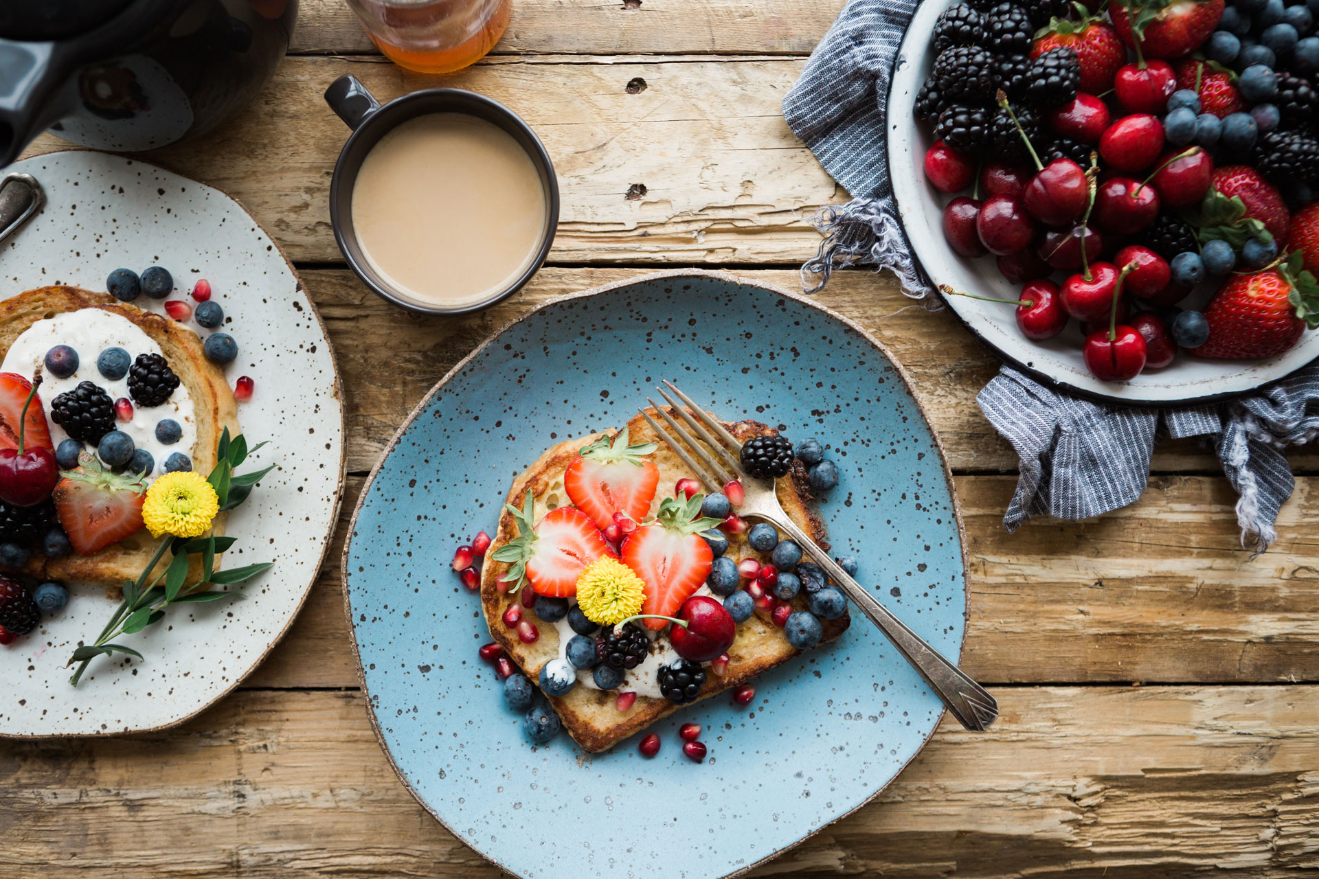 Plates of breakfast foods and berries with a coffee