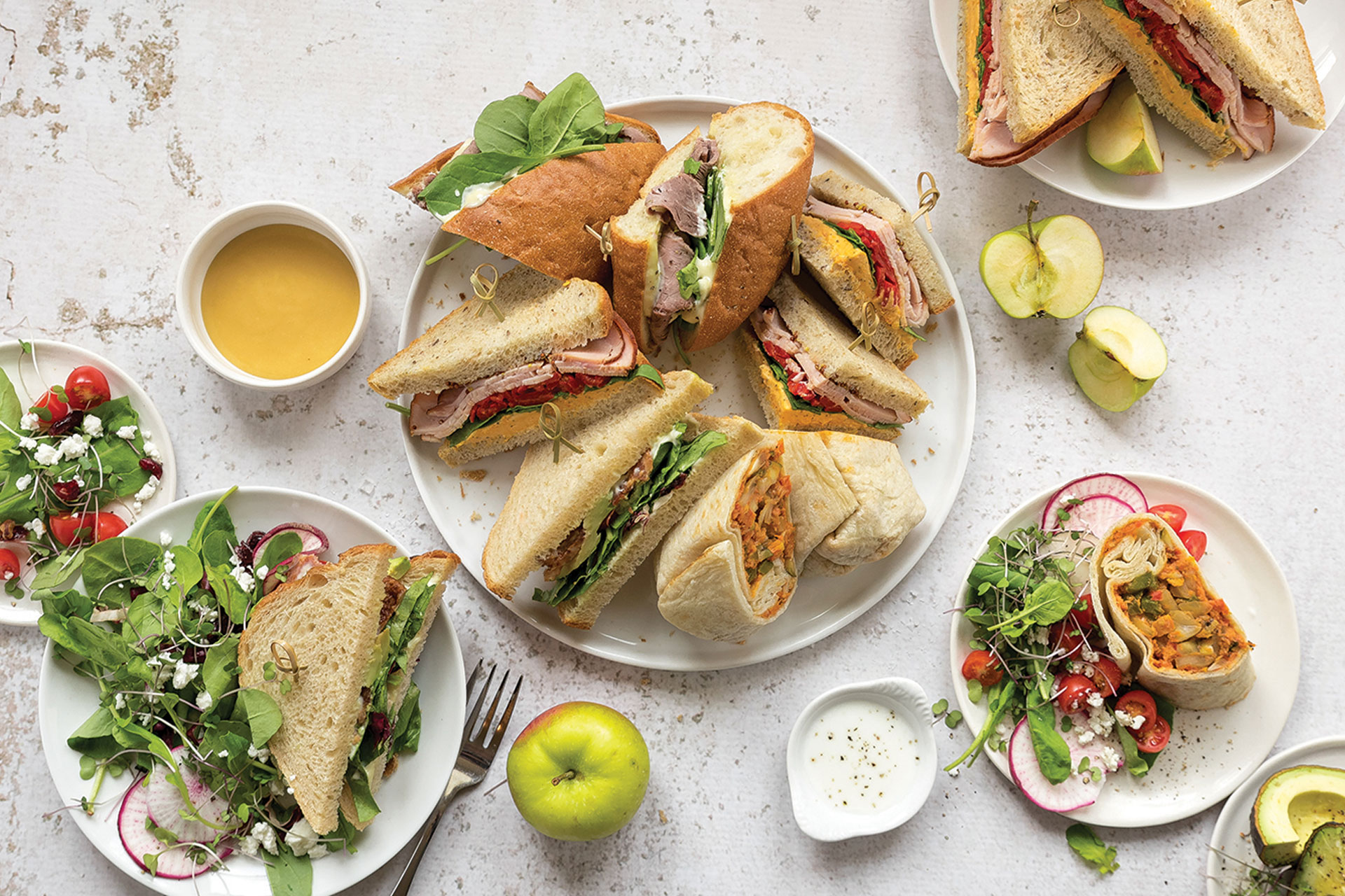 Plates of sliced sandwiches and salads with an apple