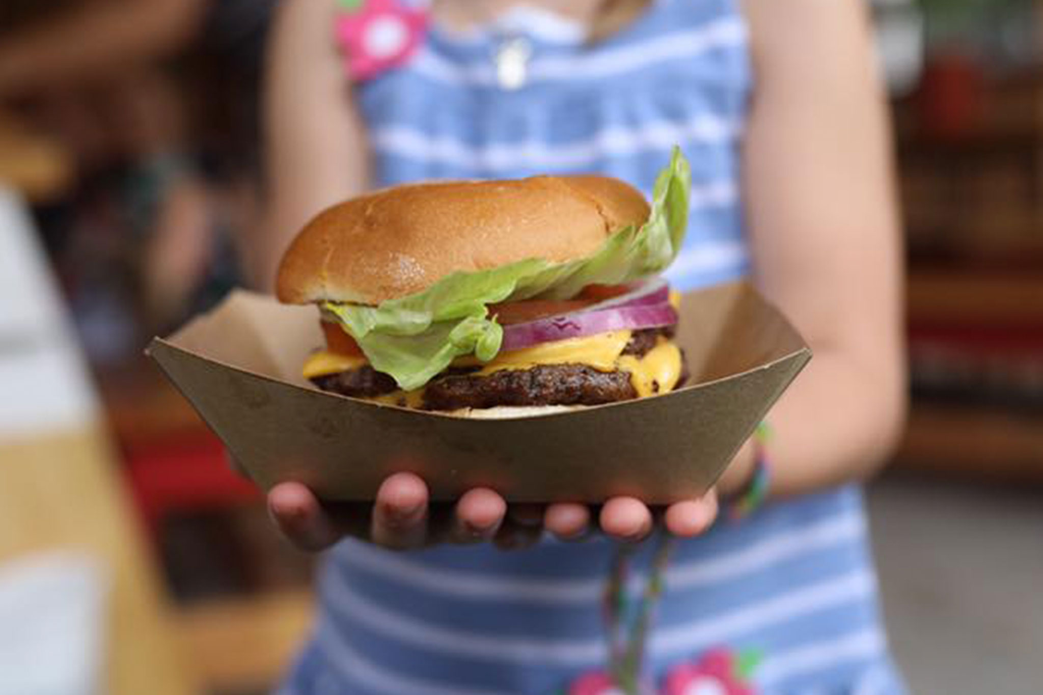 A child's hands hold a Hat Creek Burger in a takeout container