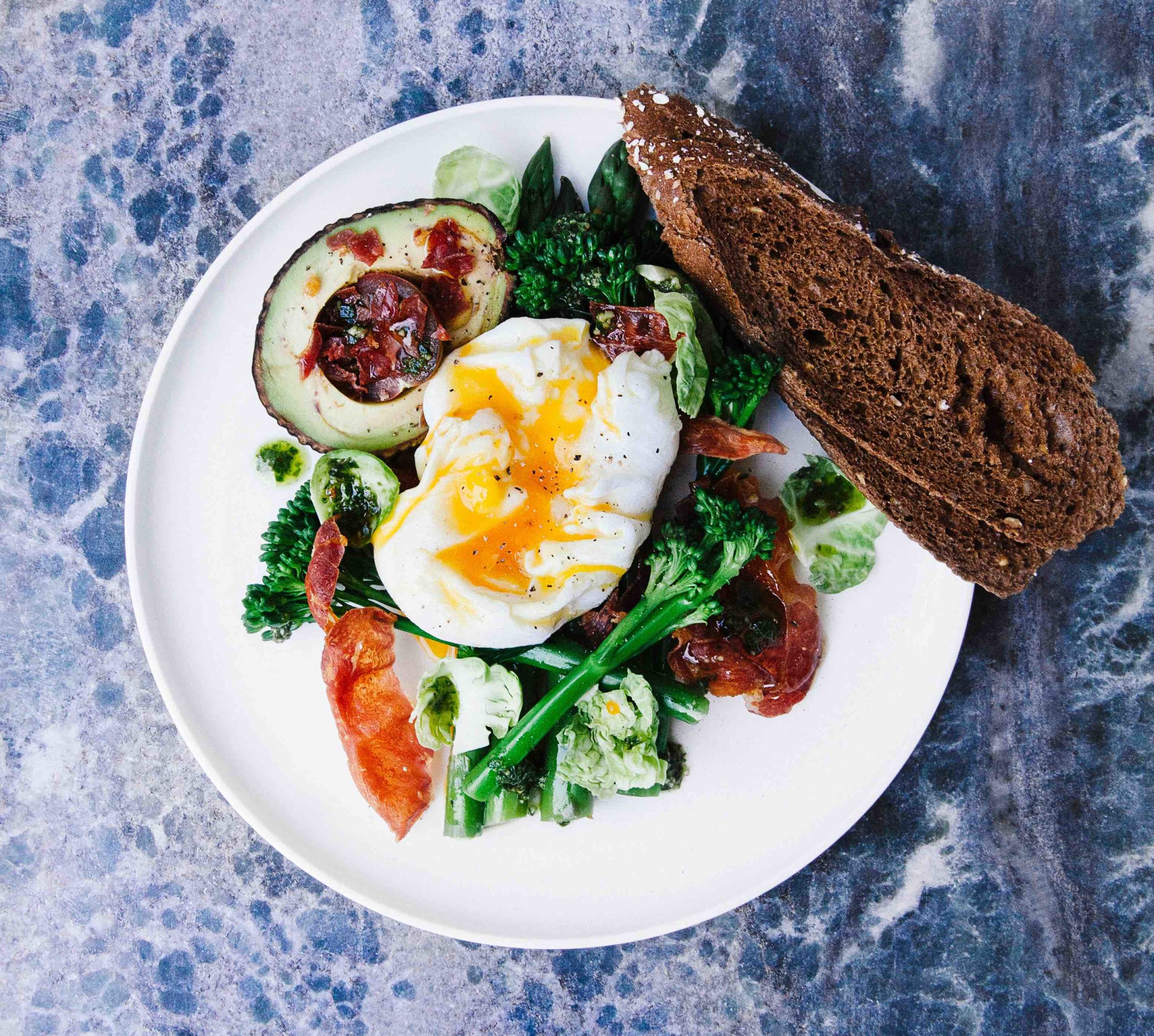 An open soft boiled egg on vegetables with avocado and toast