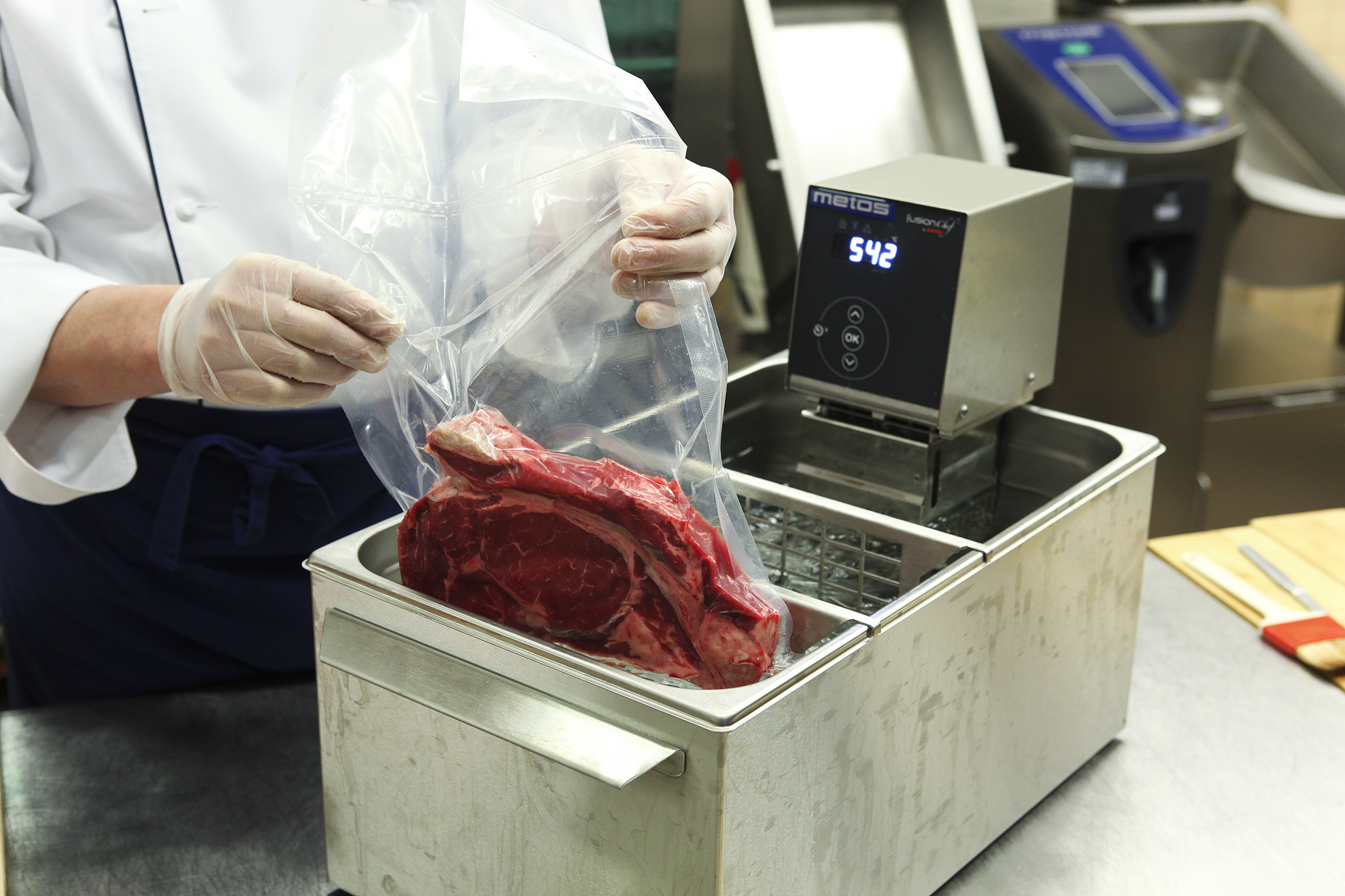 A chef putting a piece of meat in plastic into a sous vide machine