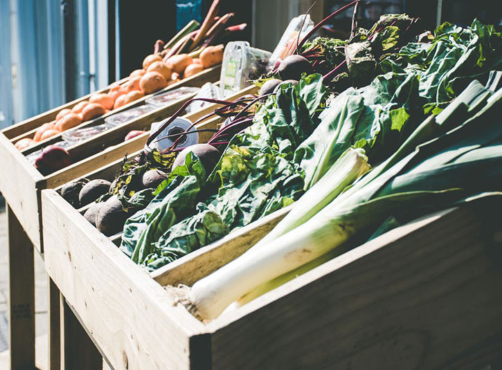 Farm stand crates with fresh vegetables on display like leeks, greens, beets, and onions