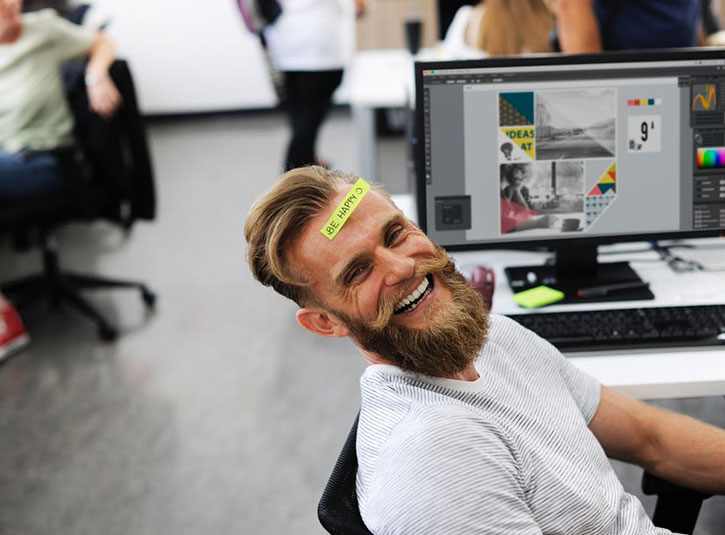 A happy employee at his desk with a 'Be Happy' post-it note on his forehead