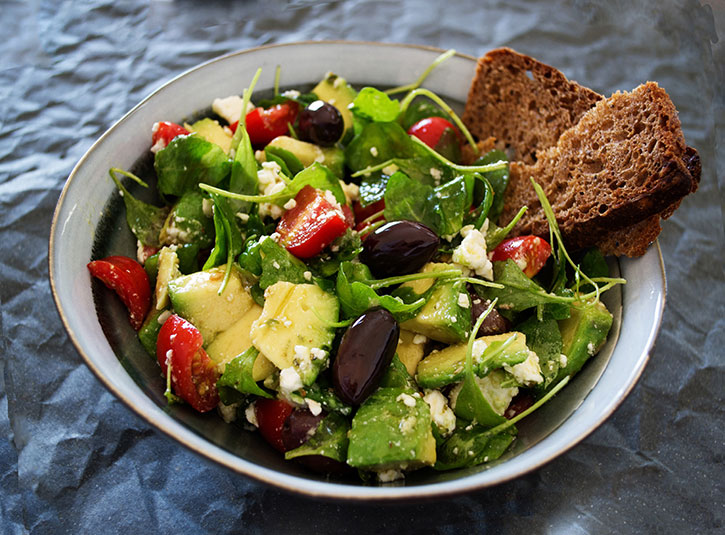 Greek arugula, avocado, olive, feta, and cherry tomato salad with bread on the side