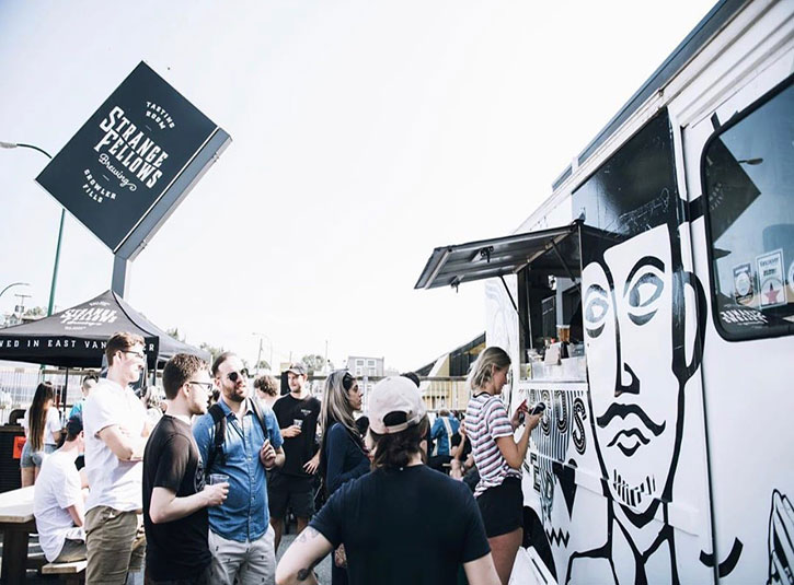 Crowd of people drinking in the Strange Fellows brewery parking lot in front of a food truck