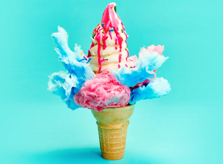 Blue and pink cotton candy and ice cream covered in pink sauce in a cone on a blue background