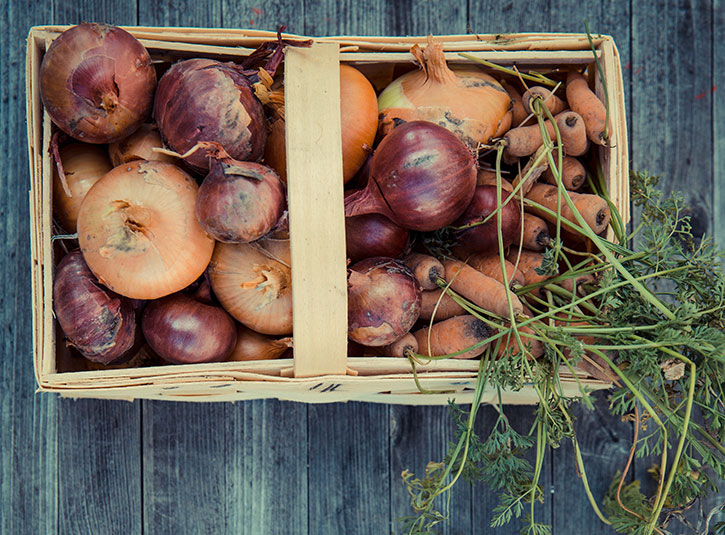 A wicker basket full of onions and carrots