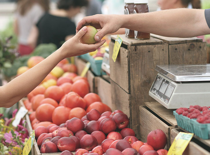 Hand passing an apple over a market stand of fruit