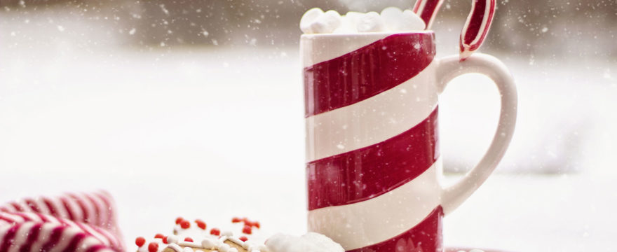 Candy cane mug with whipped cream and a candy cane in it side on a plate with festive cookies and napkins