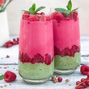 Layered smoothies in two glasses with green at the bottom, then raspberries, then a pink smoothie and more raspberries on top