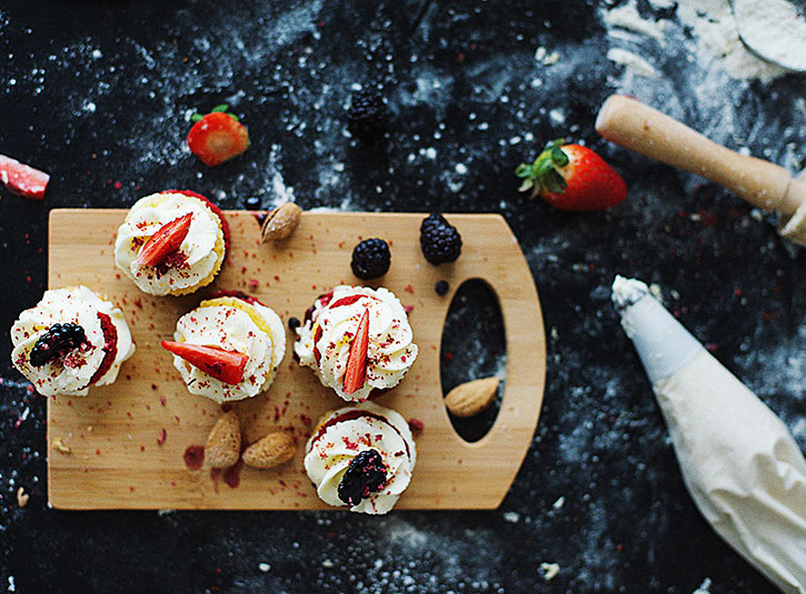 Valentine's Days cupcakes on a board on a black kitchen counter that's covered in flour, icing, and strawberries