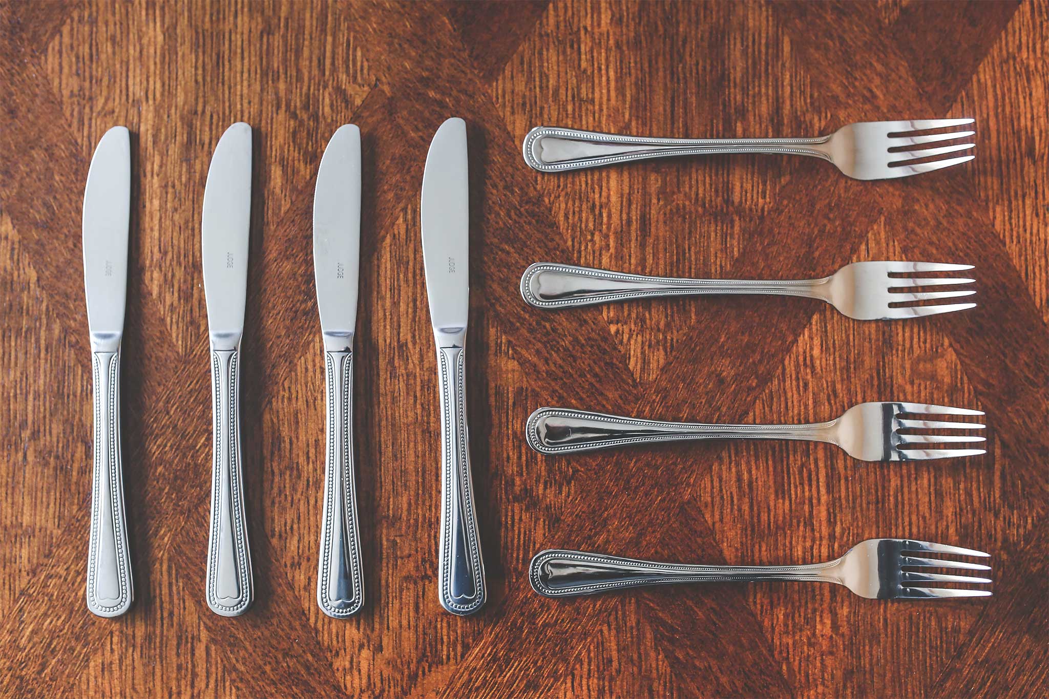 Four butter knives and four forks laid out on a wooden countertop