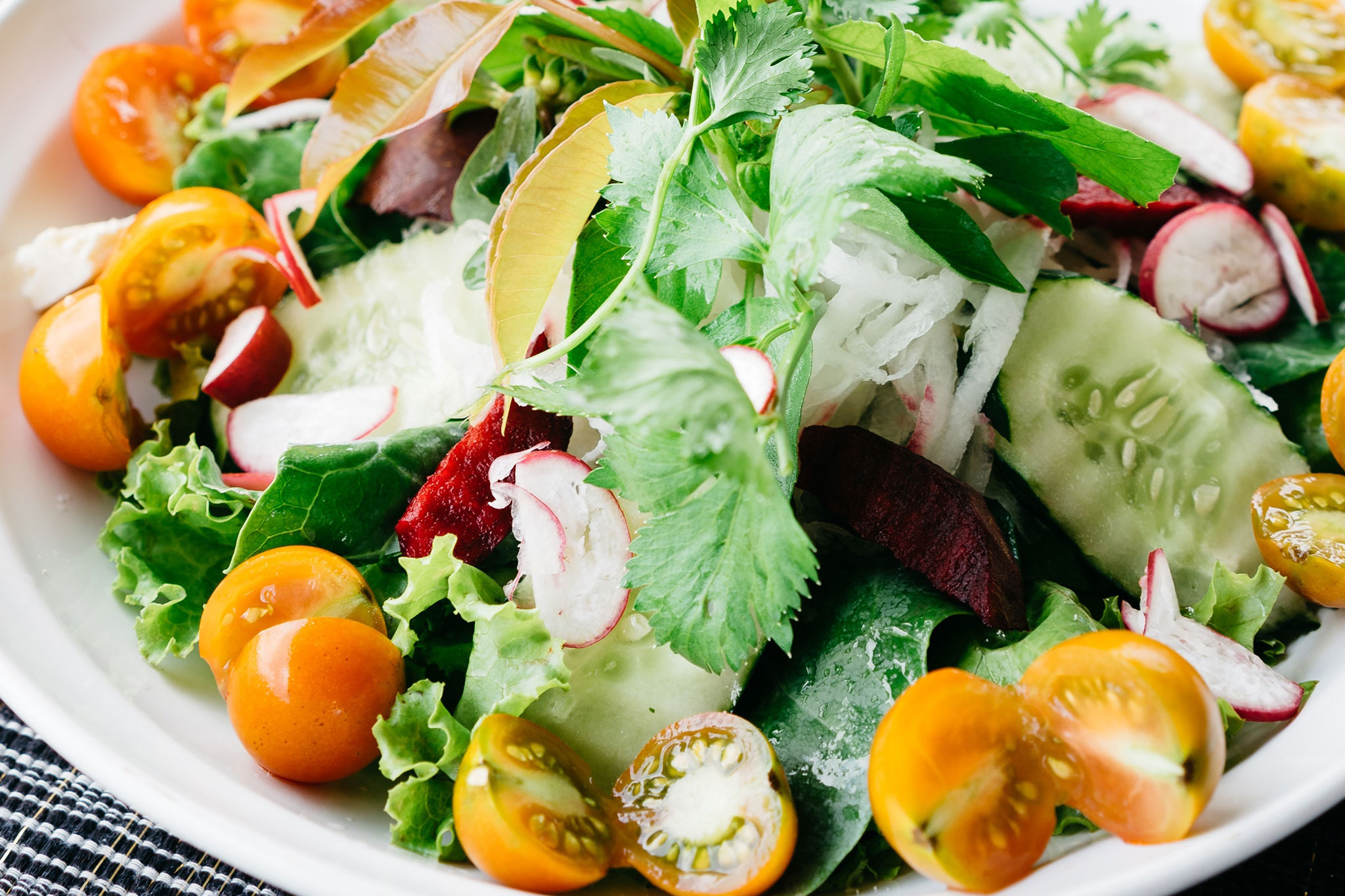 Close-up shot of a veggie salad with herbs, cherry tomatoes, cucumber, and radishes