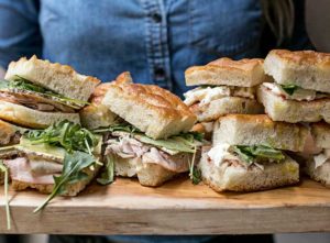 A platter full of sliced meat and arugula panini sandwiches