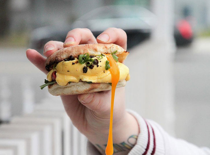 A hand holding up a Yolks breakfast sandwich that's dripping cheese