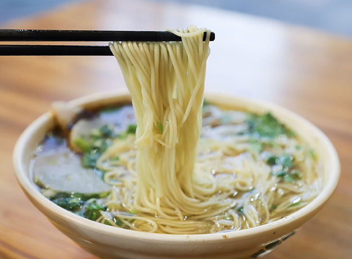 Chopsticks hold noodles out of a bowl of ramen 