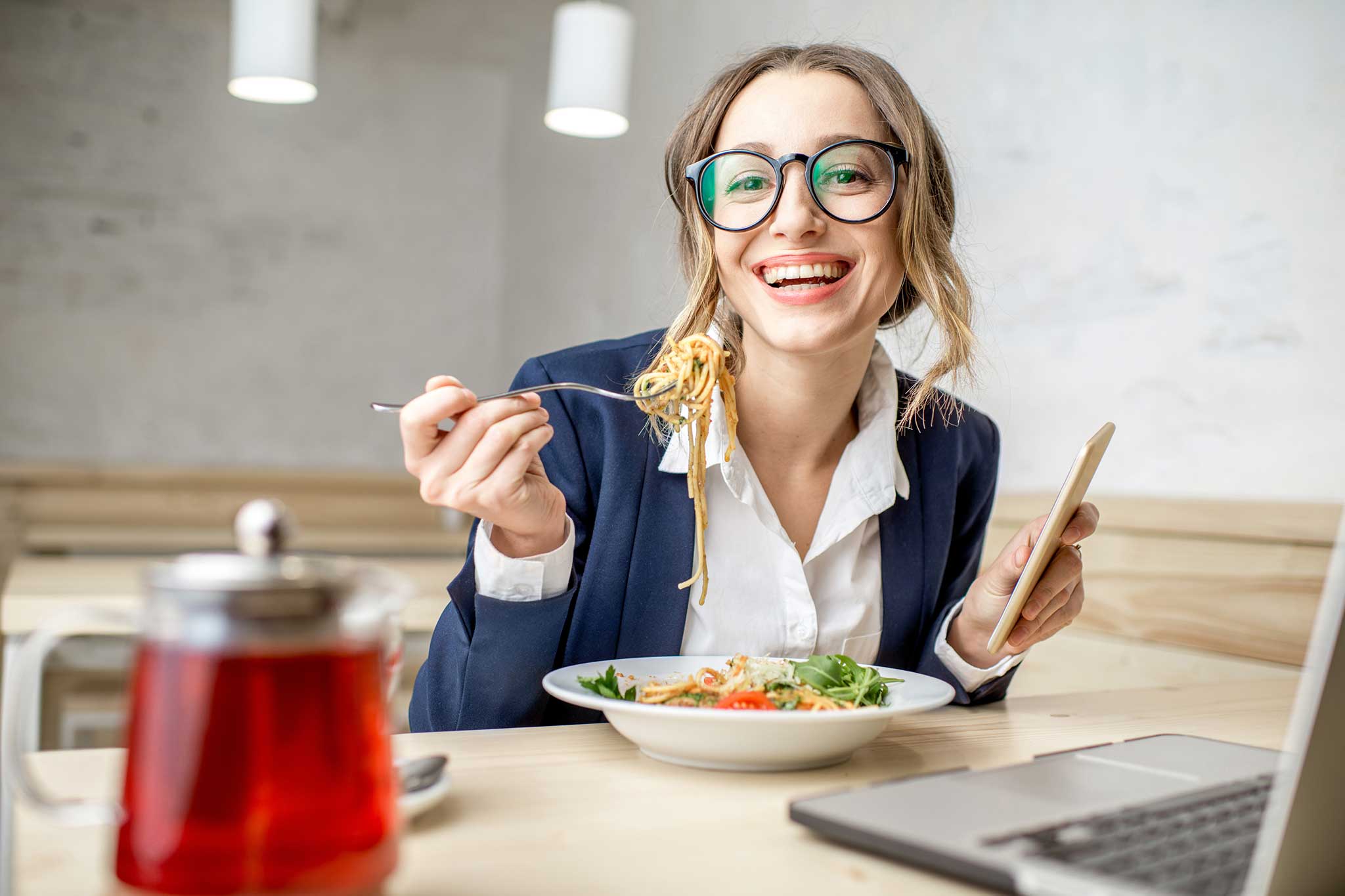 A woman smiling as she eats noodles in front of her laptop