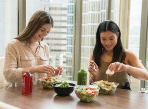 Two women eat their office lunches and juices together