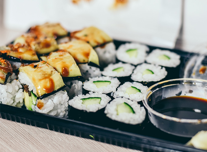 Two different sushi rolls and soy sauce on a takeout tray