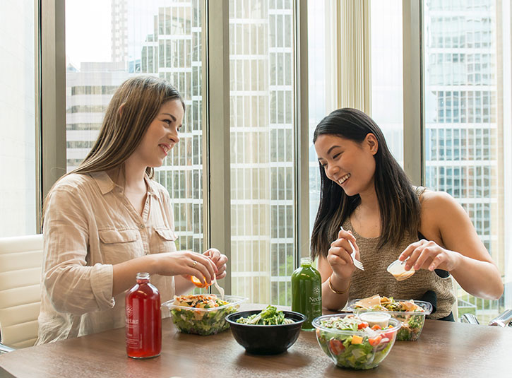 Two female employees eat their takeout lunches together
