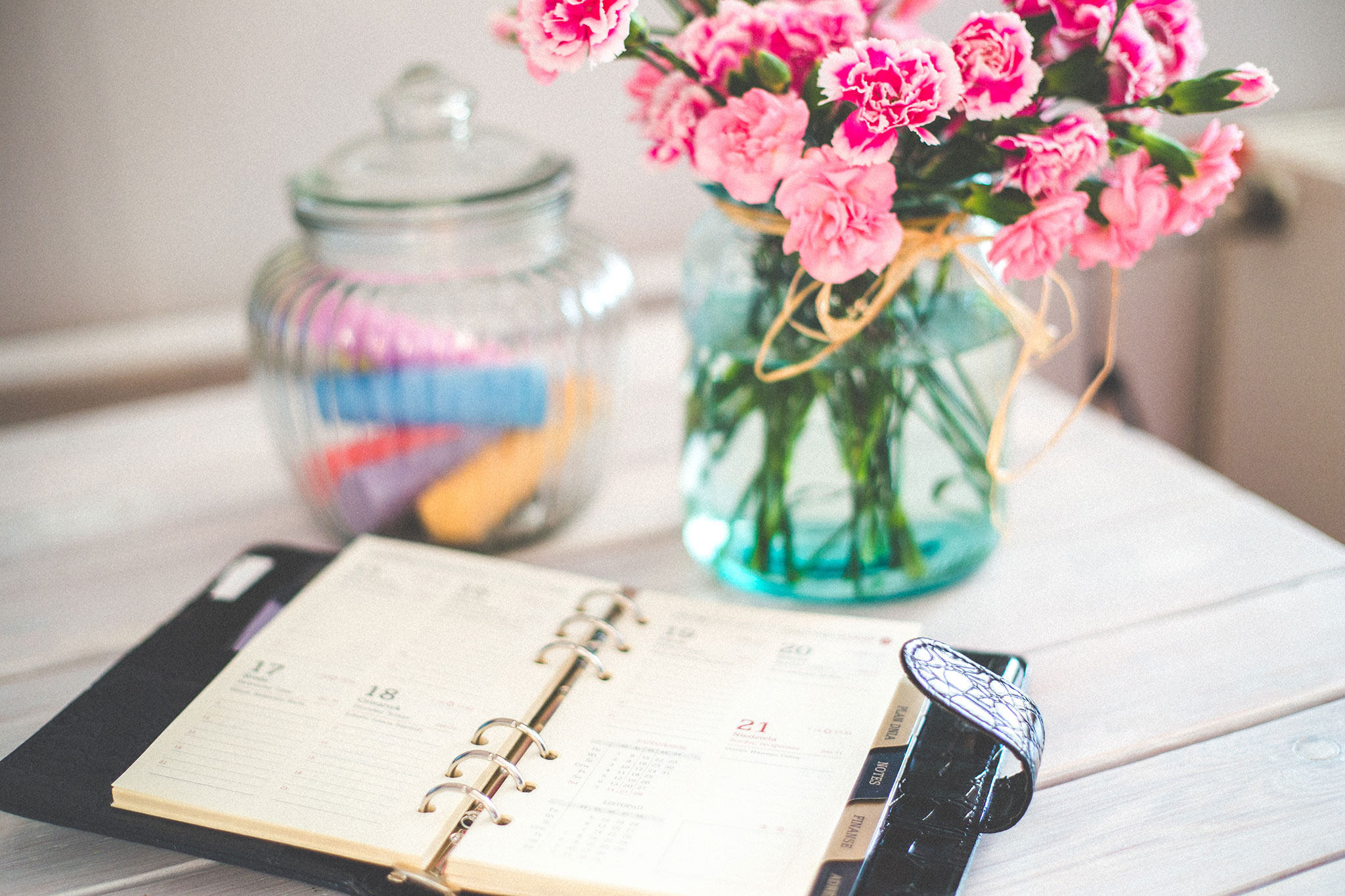 An open agenda book sits on a table with flowers and a jar full of chalk