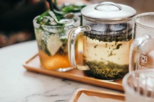 A clear glass mug full of steeping tea on tray next to an iced tea