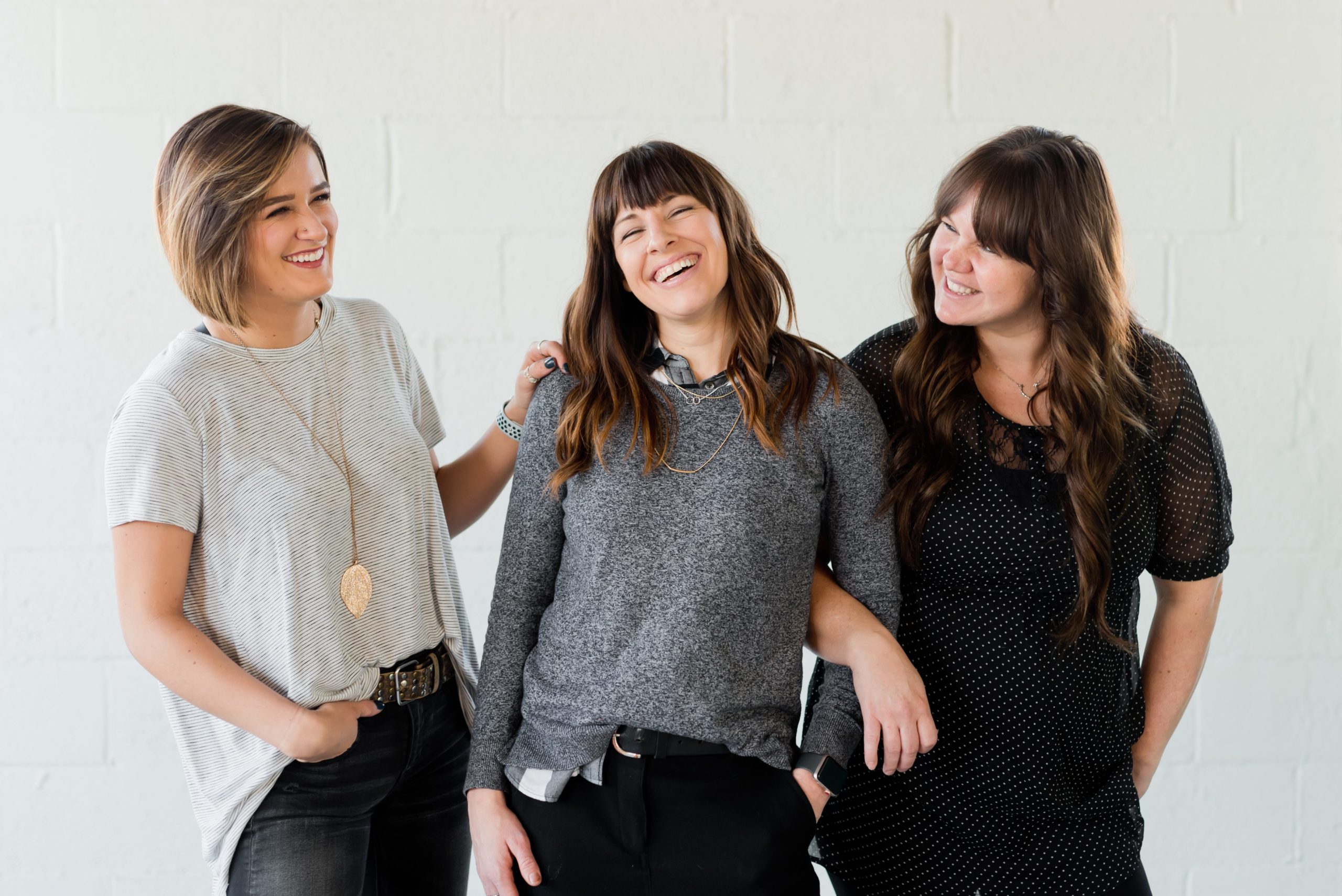 3 women smiling and standing in front of a white wall