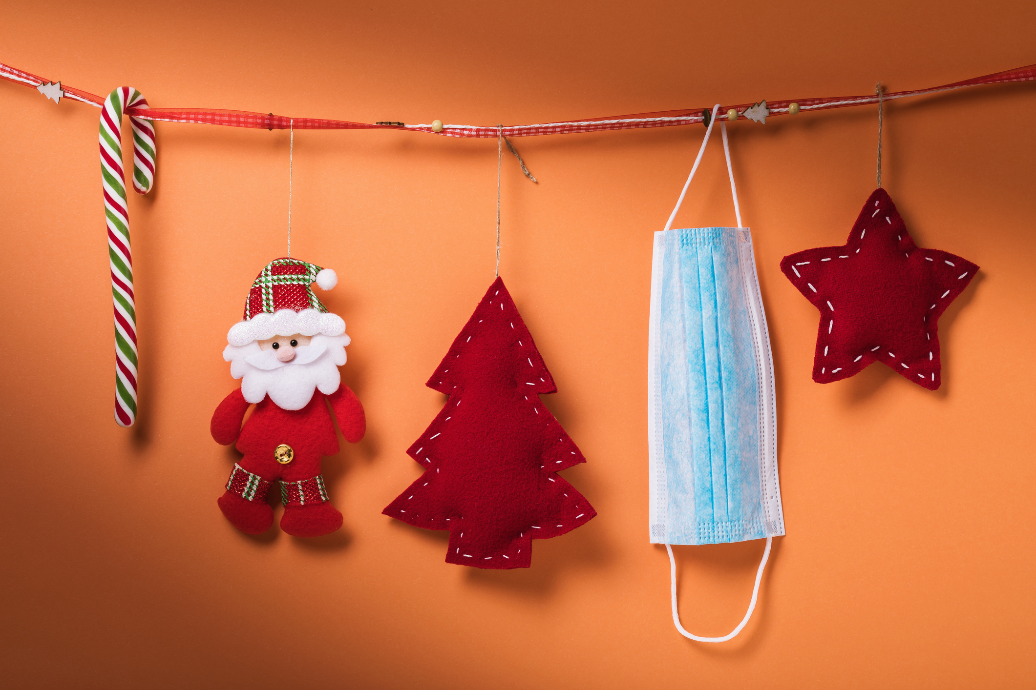 Christmas decorations and a medical mask hang on a decorative ribbon on an orange background