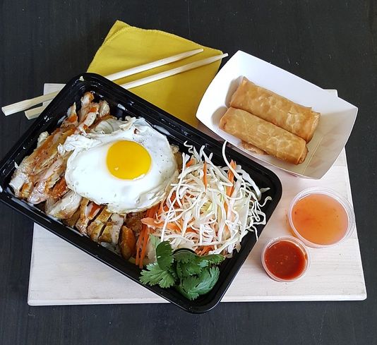 A bowl of Chicken over Rice with a side of two spring rolls alongside sweet and spicy dipping sauces.