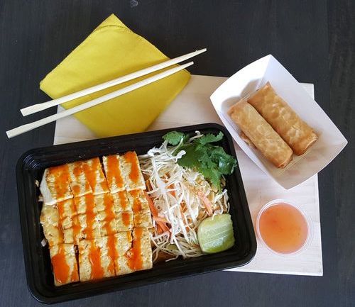 A bowl of San San Tofu Over Rice with two spring rolls alongside a sweet dipping sauce.