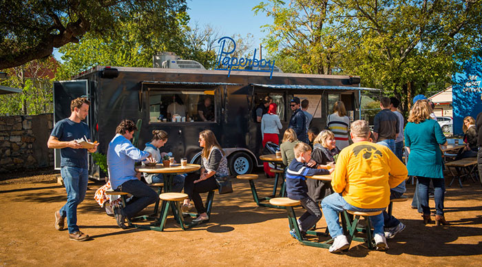 Paperboy's food truck with many people sitting at the tables in front of the truck.