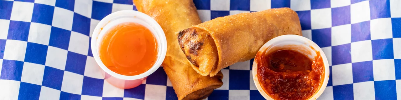 Two fried spring rolls with plum sauce and sweet and spicy sauce on the side.