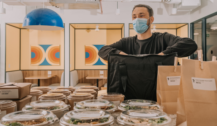 A Foodee delivery driver wearing a hospital mask while packaging multiple food containers in their delivery travel bag.