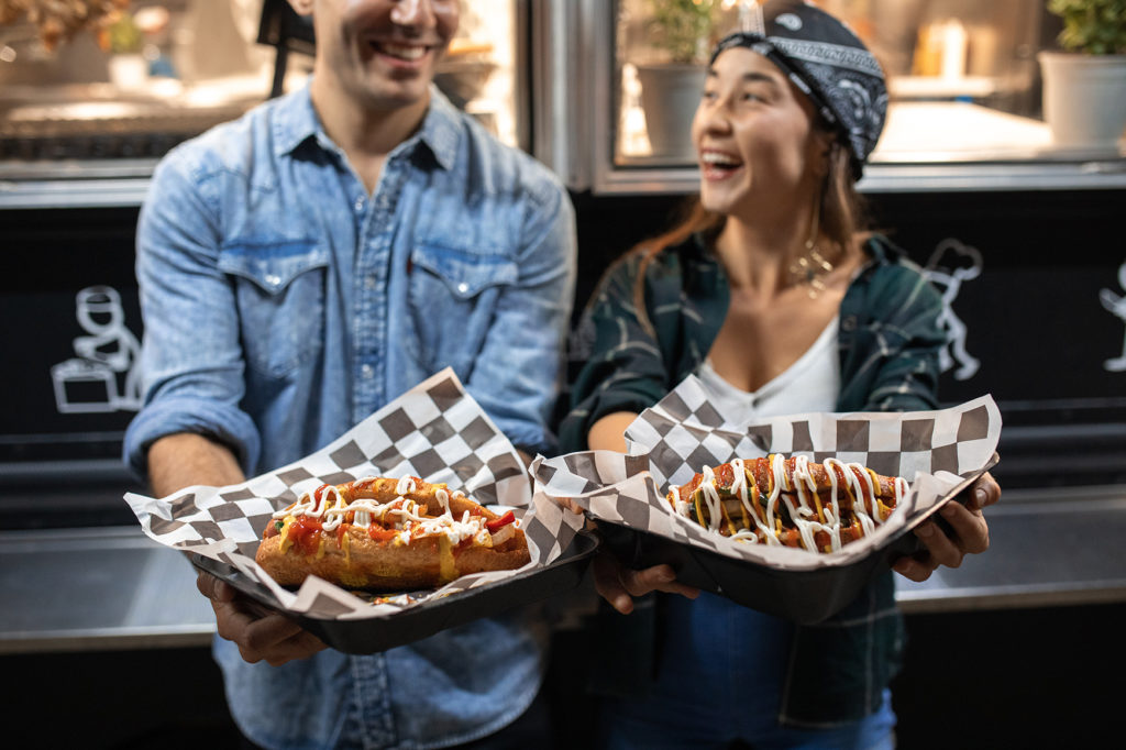 Two people holding out hot dogs