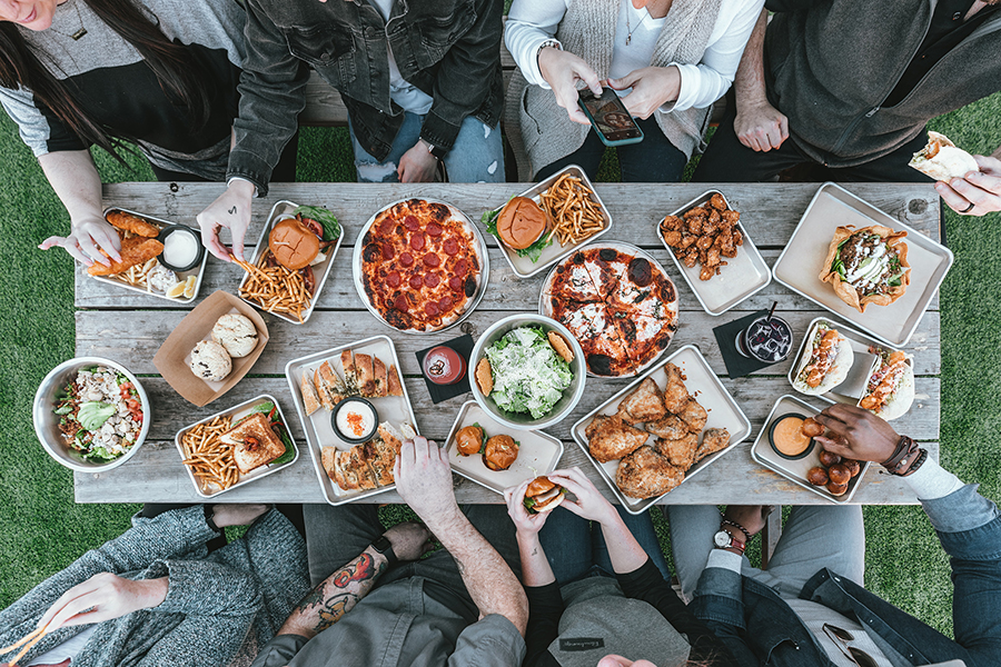 A picnic table full of food and surrounded by people