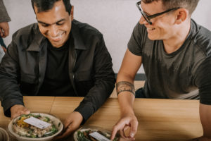 Two guys smiling as they grab their to-go meals