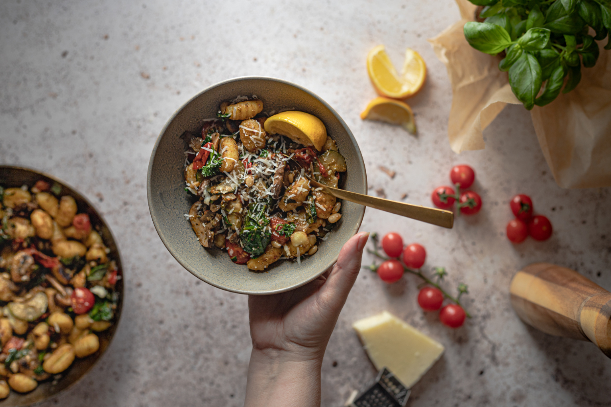 A hand holding a bowl of homecooked veggie pasta 