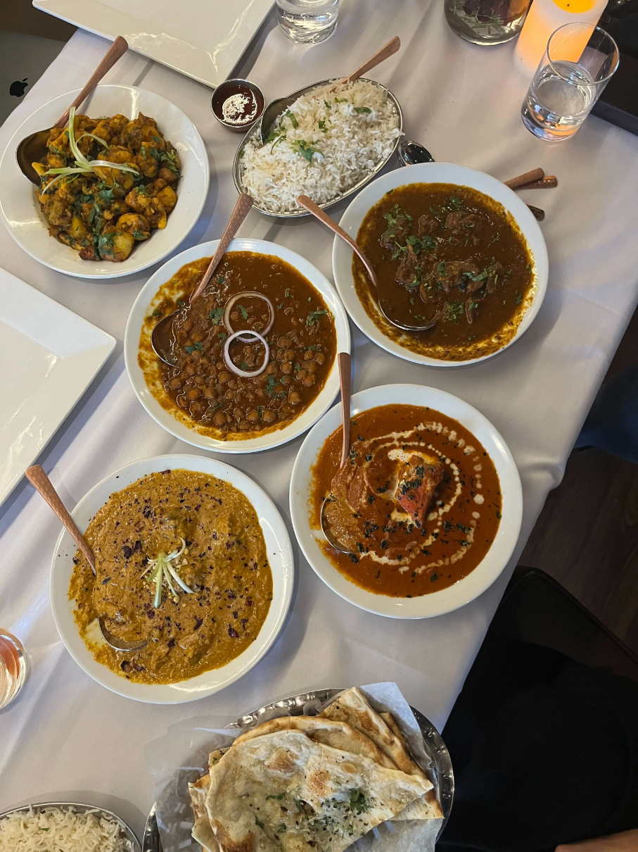 Seven platters of food on a table including: Basmati Rice, Garlic Naan, Prawn Biryani, Chicken Curry, and Chicken Karahi.