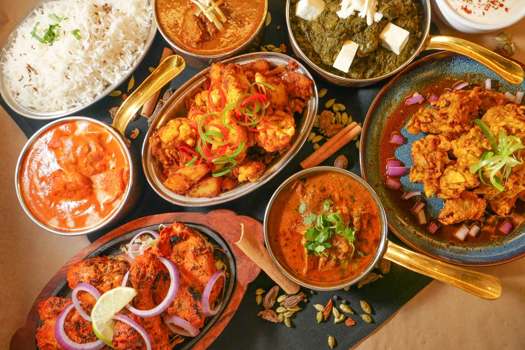 Eight food platters on a table including: Basmati Rice, Goa Fish Curry, Butter Chicken, Chicken Karahi, Palak Paneer, and Chilli Prawns.