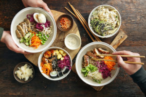 Hands reaching for healthy rice dishes in compostable bowls