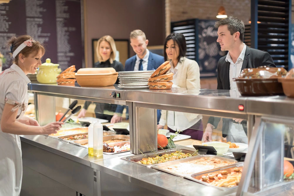 A line up of professionals awaiting to be served food at a buffet serving table.