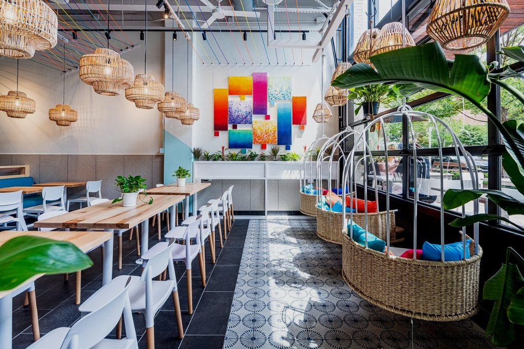 RASA's vibrant and bright restaurant interior with large open windows, swinging chairs, colourful chandeliers, and light wood tables with white chairs.