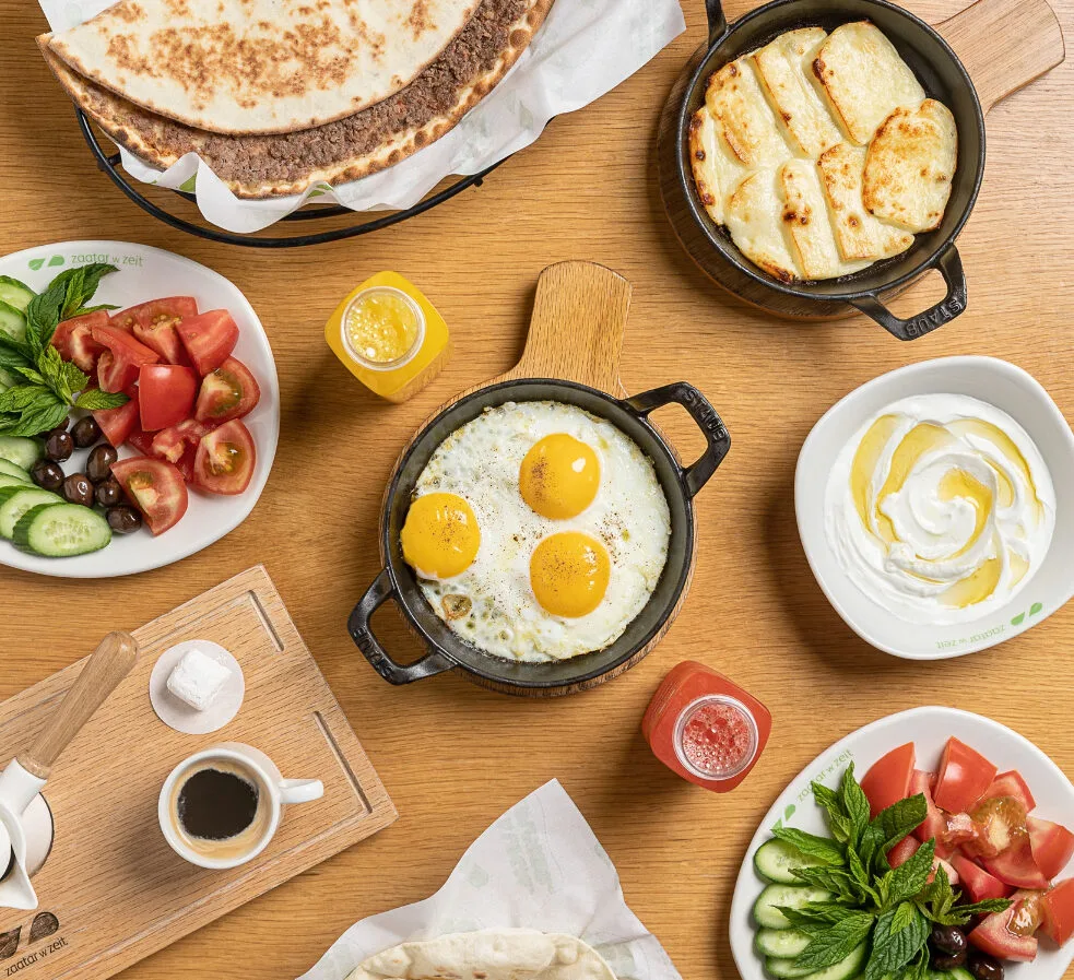 A table filled with assorted skillets and dips including: Halloumi Pan, Eggs Your Way, two Vegetable Plates, a Labneh Plate, and a Zaatar flatbread.