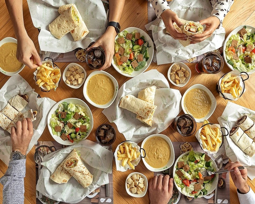 Individuals sitting at a table and sharing various food platters prepared by Zaatar.