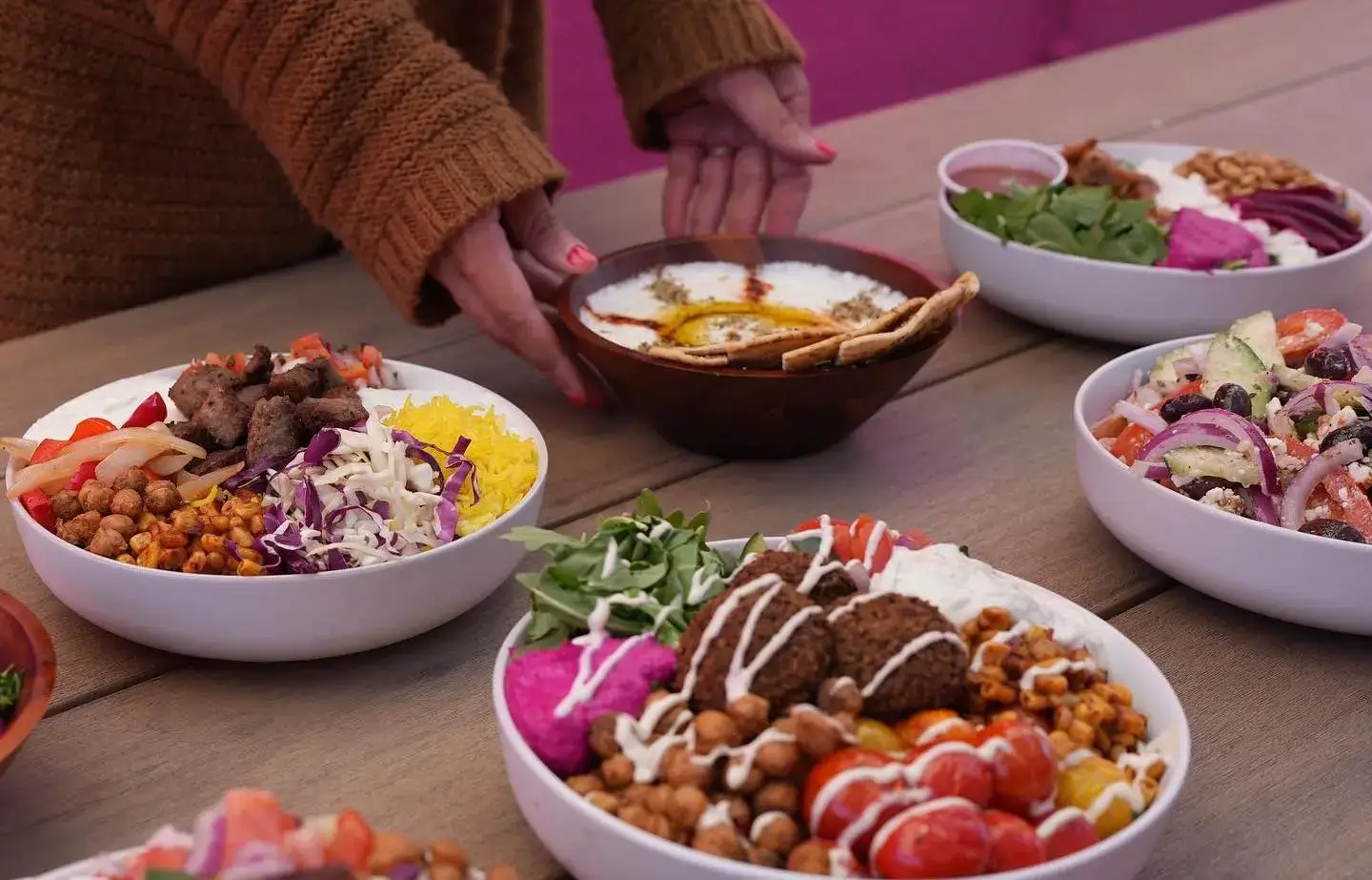 Hands reaching for one of several different falafel bowls on a table