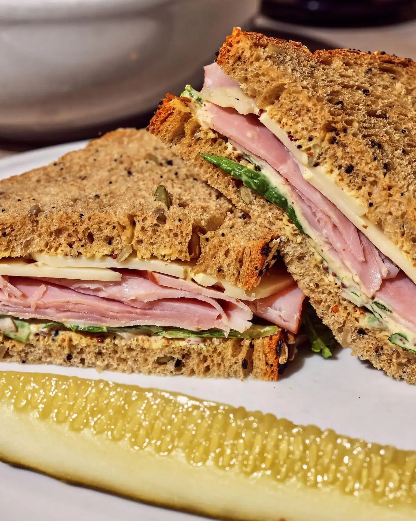 Close-up of a ham and cheese whole wheat sandwich and a sliced pickle